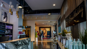 A modern boutique entrance with a marble reception desk, clothing displays, a wall mural, and hanging lights. - Hollywood Hair Salon and Spa in Centralia, IL