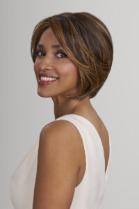 Woman with short, layered brown hair wearing a sleeveless white top, smiling and looking over her shoulder against a plain background, showcasing the effortless elegance of Jon Renau Hollywood Hair. - Hollywood Hair Salon and Spa in Centralia, IL