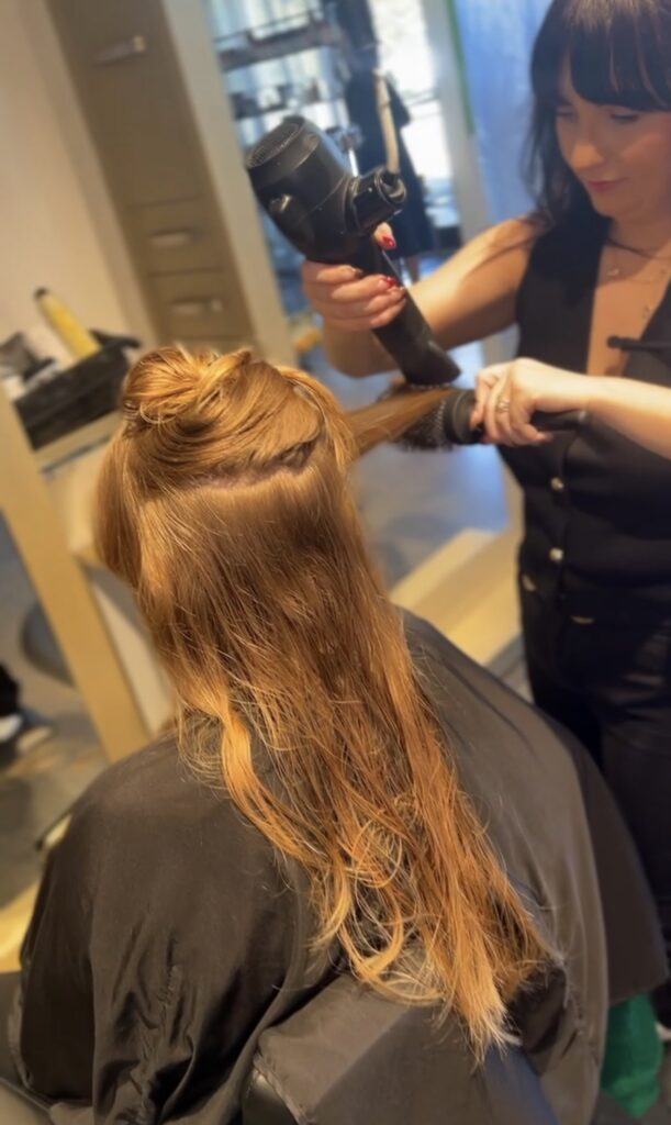 A hairdresser blow-dries a section of a woman's wet, light brown hair in a salon. - Hollywood Hair Salon and Spa in Centralia, IL