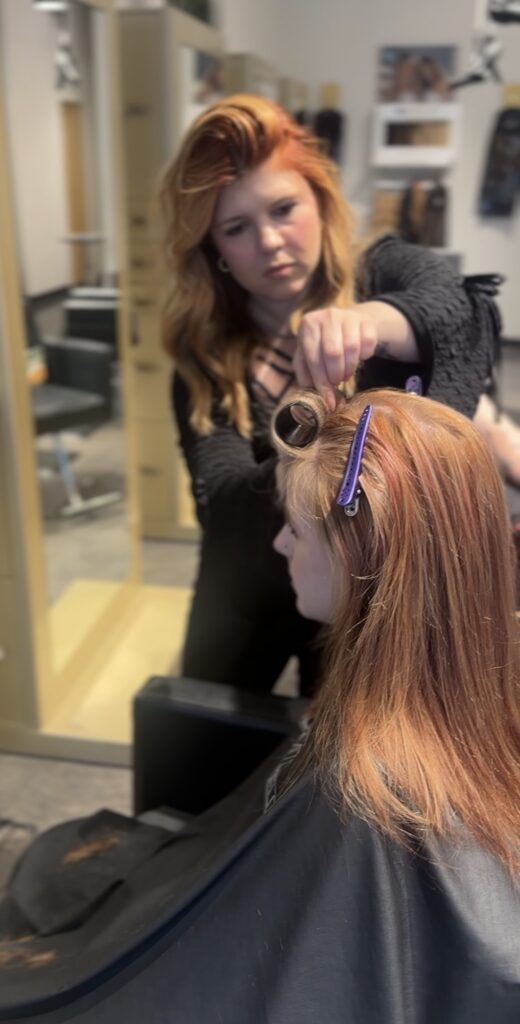 A hairstylist sections and clips a woman's hair during a salon appointment. - Hollywood Hair Salon and Spa in Centralia, IL